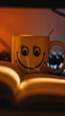 Vertical shot of a cute mug with a smiling face in front of a book