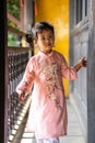 Vertical shot of a cute Vietnamese little girl in a pink ao dai walking on an old wooden balcony Royalty Free Stock Photo