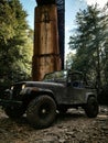 Vertical shot of dark green Jeep Wrangler by wooden construction in the woods