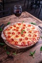 Vertical shot of a delicious cheesy pepperoni pizza with a glass of wine on a wooden table Royalty Free Stock Photo