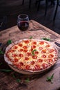 Vertical shot of a delicious cheesy pepperoni pizza with a glass of wine on a wooden table Royalty Free Stock Photo