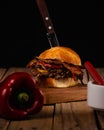 Vertical shot of a delicious hamburger and a knife in the bread and bell pepper on the tablr Royalty Free Stock Photo