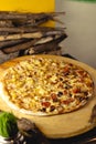 Vertical shot of a delicious pizza with sausages, cheese, pineapple, and ham on a wooden board