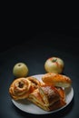 Vertical shot of delicious sesame buns or pies on white plate and yellow apple on black wooden table. Tasty unhealthy snack for Royalty Free Stock Photo