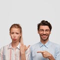 Vertical shot of dissatisfied blonde woman purses lower lip, being offended by guy. Positive unshaven hipster with Royalty Free Stock Photo