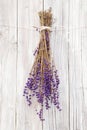 Vertical shot of dried lavenders hanging upside down in front of a white wooden background