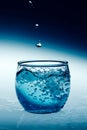 Vertical shot of drops splashing into a cup of bubbling blue liquid