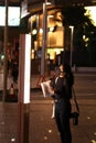 Vertical shot of an Eastern Asian woman in a mask with a map looking at a banner in the evening