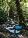 Vertical shot of an empty blue foldable camping chair in a forest, facing a water stream.