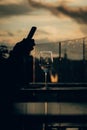 Vertical Shot Of An Empty Glass And A Hand Silhouette Holding A Phone With Sunset In The Background