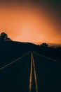 Vertical shot of an empty road with yellow indicator lines against an orange dusk sky