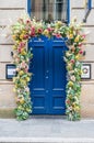 Vertical shot of an entrance of the building with blue door decorated with colorful flowers