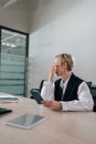 Vertical shot of exhausted middle-aged businesswoman using mobile phone at office desk, feeling discomfort from dry Royalty Free Stock Photo