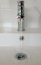 Vertical shot of a faucet on the sink with water running down and going into the drain Royalty Free Stock Photo