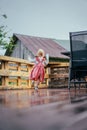 Vertical shot of a female child running on the deck of a house wearing a pink dress