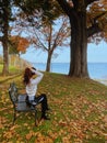 Vertical shot of a female sitting on a bench and fixing her hair near a lake shore Royalty Free Stock Photo