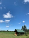 Vertical shot of a field with a wooden small house and blue sky in the background Royalty Free Stock Photo