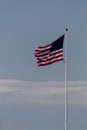 Vertical shot of the flag of the USA wavering on the air pinned to a white pole