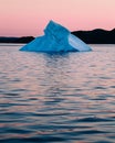 Vertical shot of a floating iceberg in an ocean and the silhouette of hills at the sunset