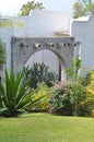 Vertical shot of flowers and plants near a small stone arch beside a white wall Royalty Free Stock Photo