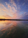 Vertical shot fluffy colorful clouds reflecting the sunset on the lake water surface. Calm, idyllic evening scene with lots of Royalty Free Stock Photo