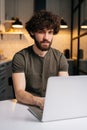 Vertical shot of focused bearded young freelancer male using typing on laptop keyboard, writing email or message sitting Royalty Free Stock Photo