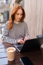 Vertical shot of focused beautiful young woman sitting at table with laptop in outdoors cafe working online. Female Royalty Free Stock Photo