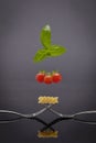 Vertical shot of forks crossed each other holding pasta, tomato and mint above on black background