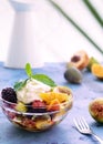 Vertical shot of fresh healthy mixed fruit salad with yogurt and mint on blue table surface against white background. Close-up. Royalty Free Stock Photo