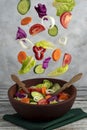 Vertical shot of a fresh vegetable salad with vegetables falling through the air into a wooden bowl