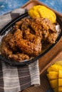 Vertical shot of fried chicken wings with cut mangos on a board under the lights Royalty Free Stock Photo