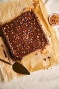 Vertical shot of a fudge brownie on a brown surface next to a bowl of walnuts and a large spoon