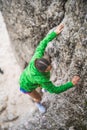 Vertical shot of a girl in a green coat climbing cliffs