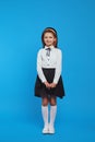 Vertical shot of girl kid in school uniform, posing adorable over blue wall Royalty Free Stock Photo