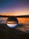 Vertical shot of a glass ball on a sand surface with the reflection of beautiful sea during sunset