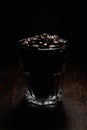 Vertical shot of a glass cup filled with coffee beans on a wooden surface with a black background Royalty Free Stock Photo