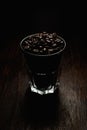 Vertical shot of a glass cup filled with coffee beans on a wooden surface with a black background Royalty Free Stock Photo