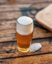 Vertical shot of a glass of foamy beer on a wooden beach table