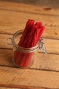 Vertical shot of glass jar with red licorice sticks on a wooden background