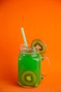 Vertical shot of a glass of kiwi drink with fresh kiwis on an orange background