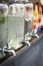 Vertical shot of glass lemonade dispensers on a wooden table with colorful plastic cups next to it Royalty Free Stock Photo
