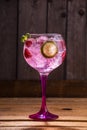 Vertical shot of a glass of pink tonic and gin with raspberries and lime on a wooden table