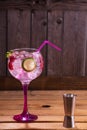 Vertical shot of a glass of pink tonic and gin with raspberries and lime on a wooden table