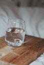 Vertical shot of a glass of water with a wooden board on white fabric