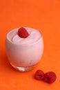 Vertical shot of a glass of yogurt with raspberry on an orange background
