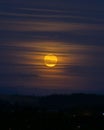 Vertical shot of a glowing yellow moon behind thin clouds in the evening