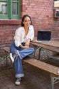 Vertical shot of good-looking asian woman with laptop, sitting in outdoor cafe, drinking coffee and smiling, laughing Royalty Free Stock Photo