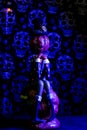 Vertical shot of a Halloween figurine against a grungy skull wall with purple lights background