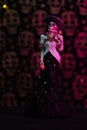 Vertical shot of a Halloween figurine against a grungy skull wall with purple lights background