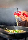 Vertical shot of a hand crushing garlic with a kitchen tool and pouring it over the stew in a pan Royalty Free Stock Photo